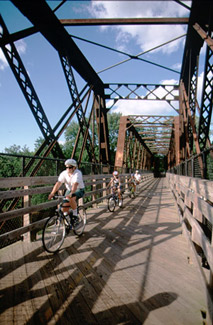 Bicycles crossing an old iron railroad bridge which has been converted as part of a rail trail with wooden decking