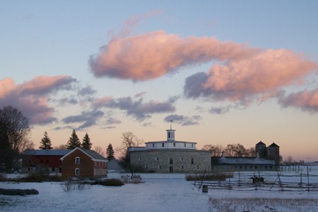 round barn and other farm buildings under a pink-clouded dusk sky
