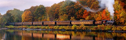 Steam train running beside the Connectoicut River with fall foliage behind and reflected in the water